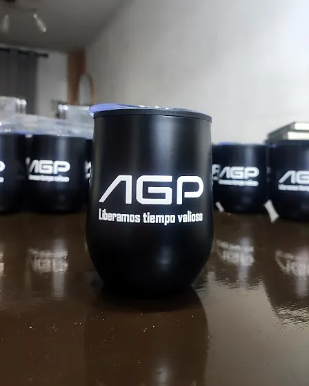 Vaso térmico negro con el logo AGP y la frase «Liberamos tiempo valioso», con más vasos iguales detrás