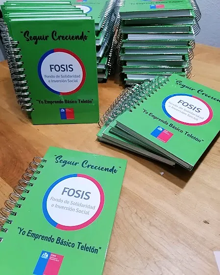 Agendas verdes anilladas de FOSIS «Seguir creciendo», apiladas sobre una mesa