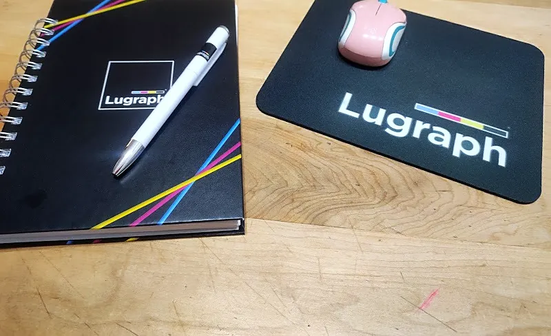 Agenda negra con lápiz blanco y mousepad negro con el logo de Lugraph