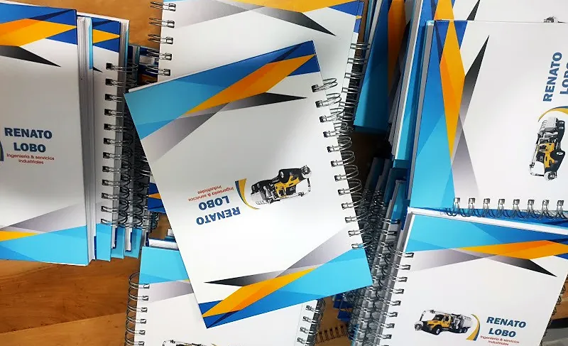 Agendas anilladas de Renato Lobo, con tapa blanca y franjas azules y naranjas, apiladas