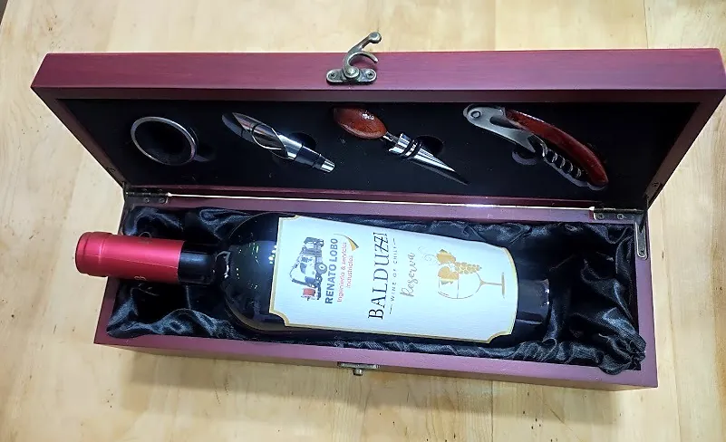 Caja de madera con accesorios de vino y una botella con etiqueta personalizada de Renato Lobo