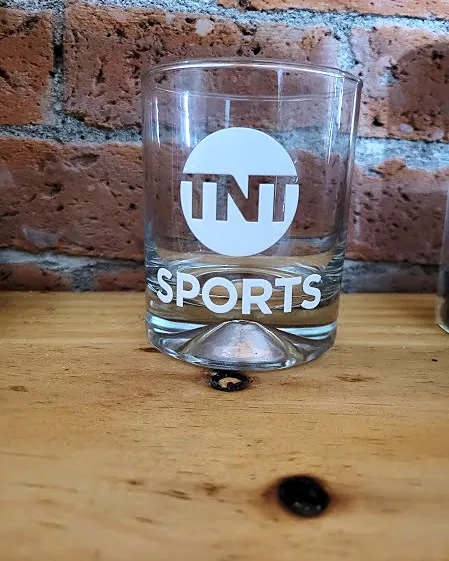 Vaso de vidrio con el logo de TNT Sports en blanco, frente a un muro de ladrillo